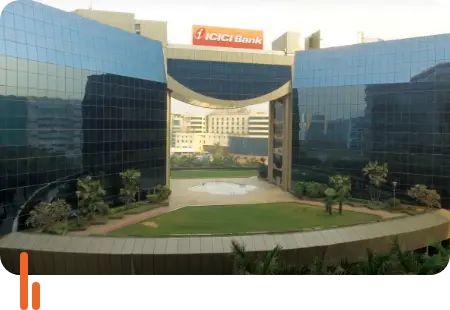 A photograph of the ICICI Bank corporate building, featuring modern architecture with reflective glass panels and a spacious courtyard, symbolizing the bank's presence and corporate identity.