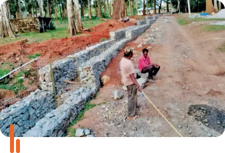 A photograph showing a gabion structure constructed at Nagarahole Tiger Reserve in Karnataka, with two workers on-site. The structure is made of wire mesh filled with rocks, used for erosion control and habitat protection in the reserve.