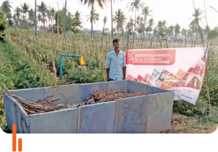 A millet farmer standing beside a vermicompost slab at D.M. Samudra village in Chamarajanagar district, Karnataka, with an ICICI Foundation Rural Livelihood banner in the background.