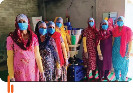 Women in traditional attire and protective face masks processing mustard oil using a cold press extraction machine at Adampur village in Hisar district, Haryana.